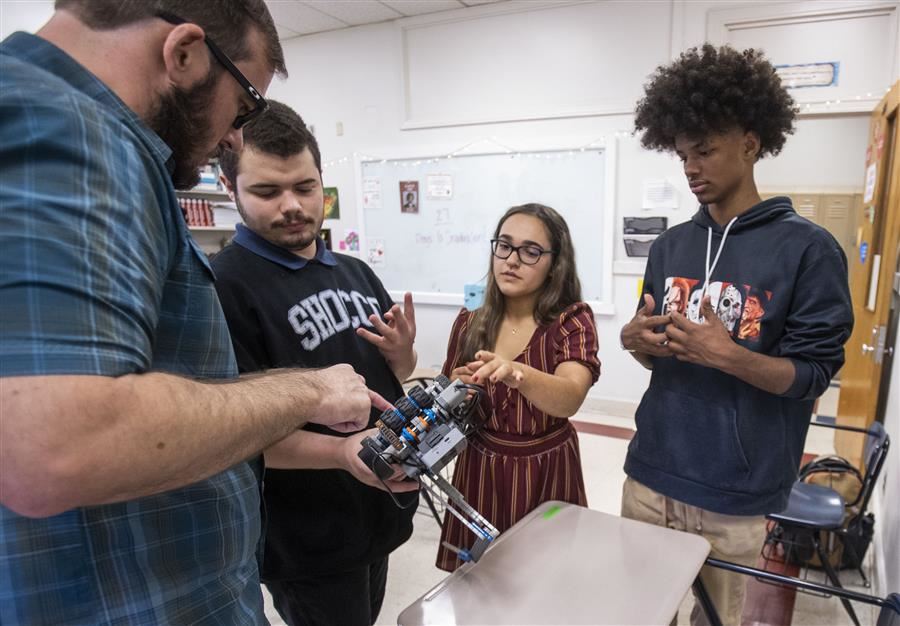  Three students and an instructor in discussion as they look over a robot.